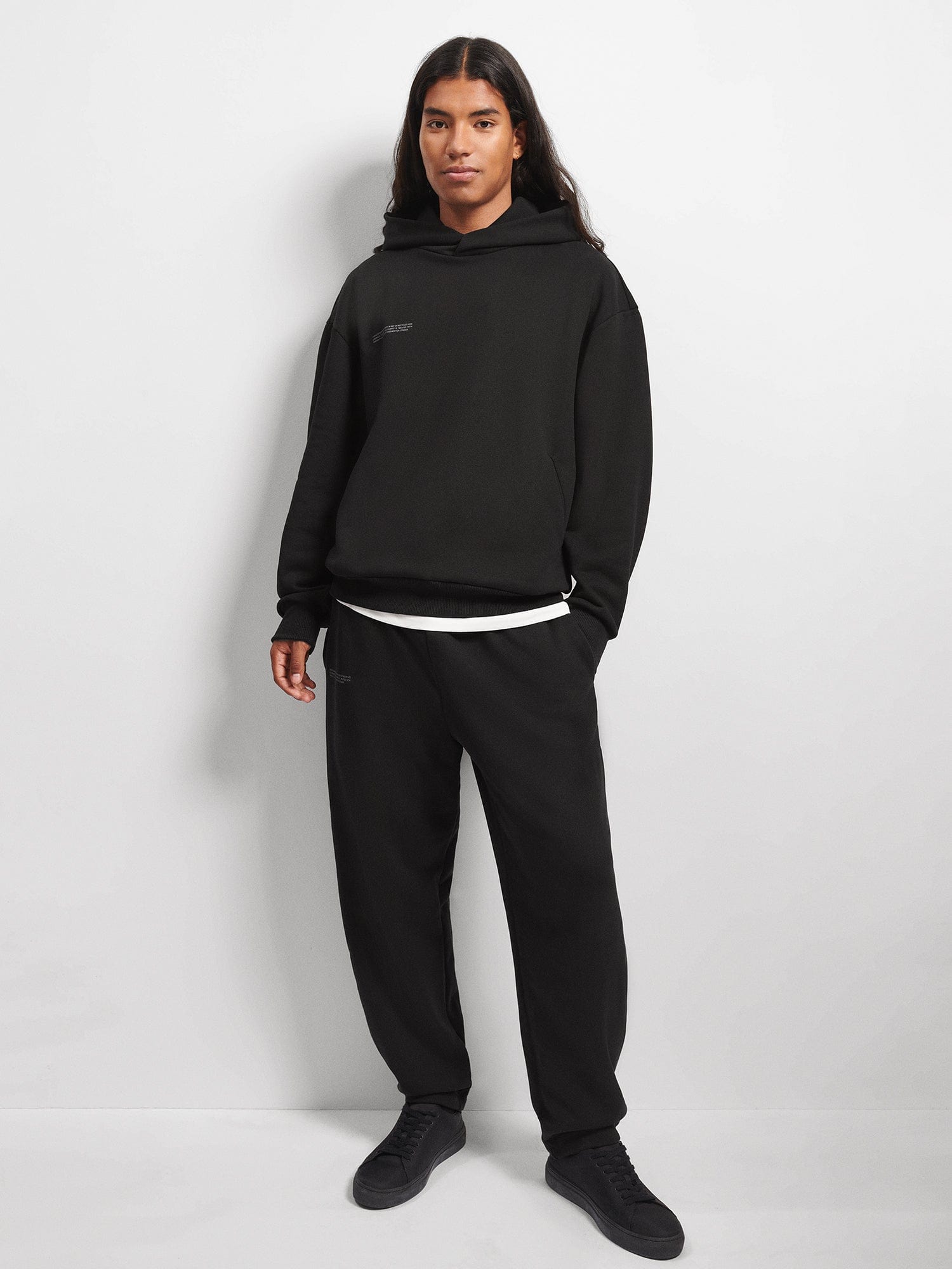 Black oversized hooded sweatshirt and black relaxed-fit sweatpants on a model. Premium cotton fleece loungewear set