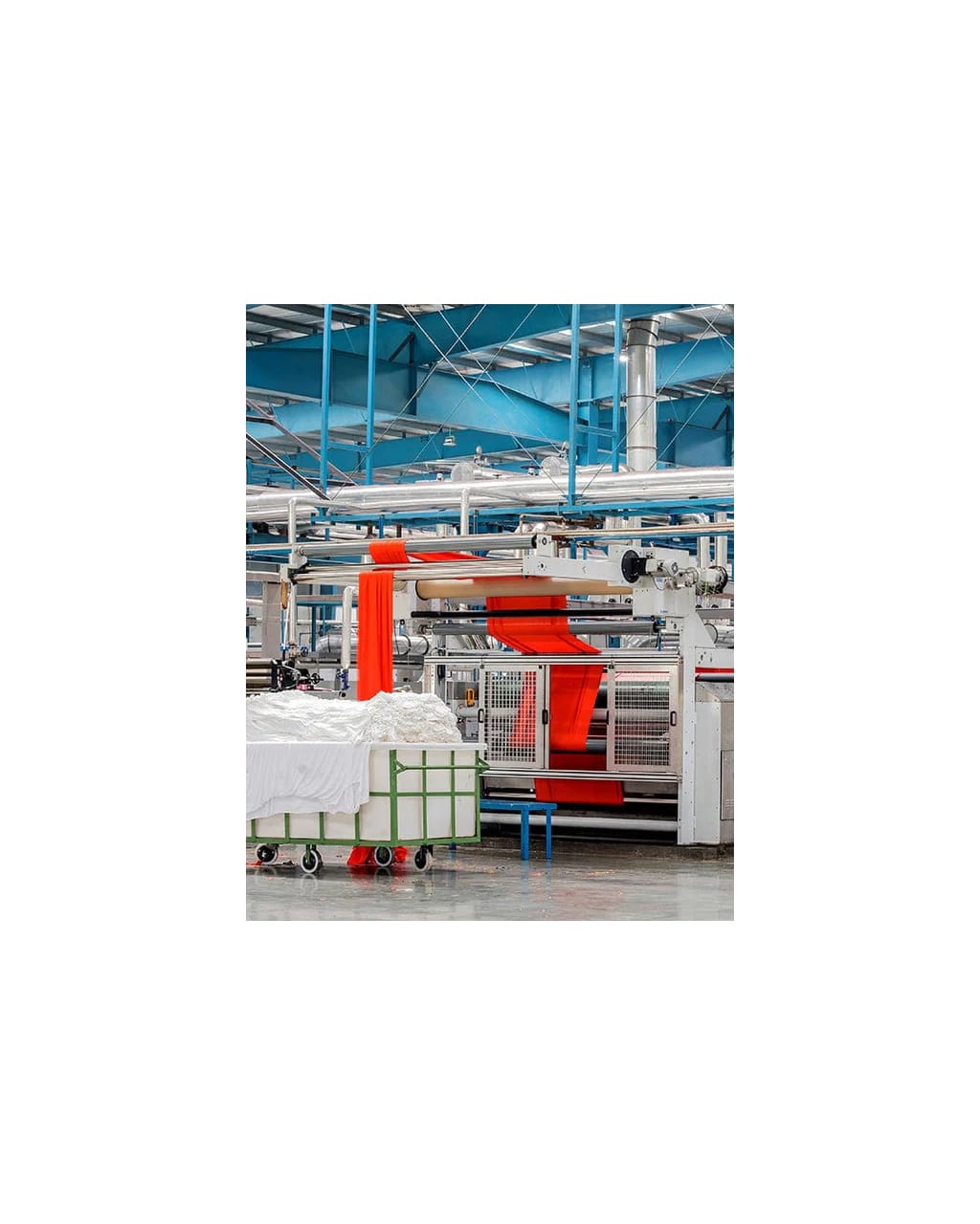 Textile manufacturing facility with machinery processing vibrant orange fabric, alongside a cart filled with white raw garment material