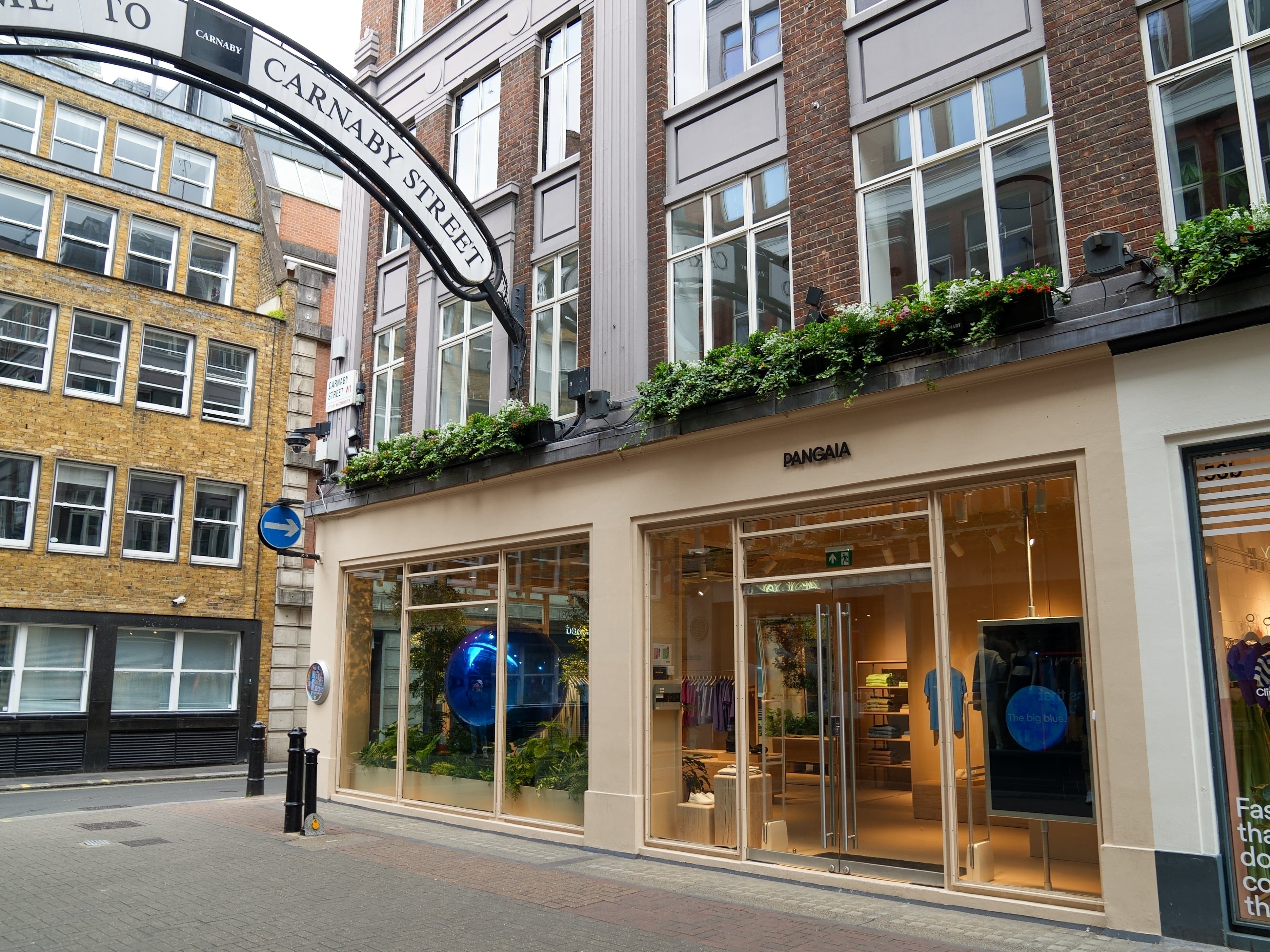 Pangaia retail store on Carnaby Street London. Exterior view showing large windows, colorful clothing displays, and brick buildings