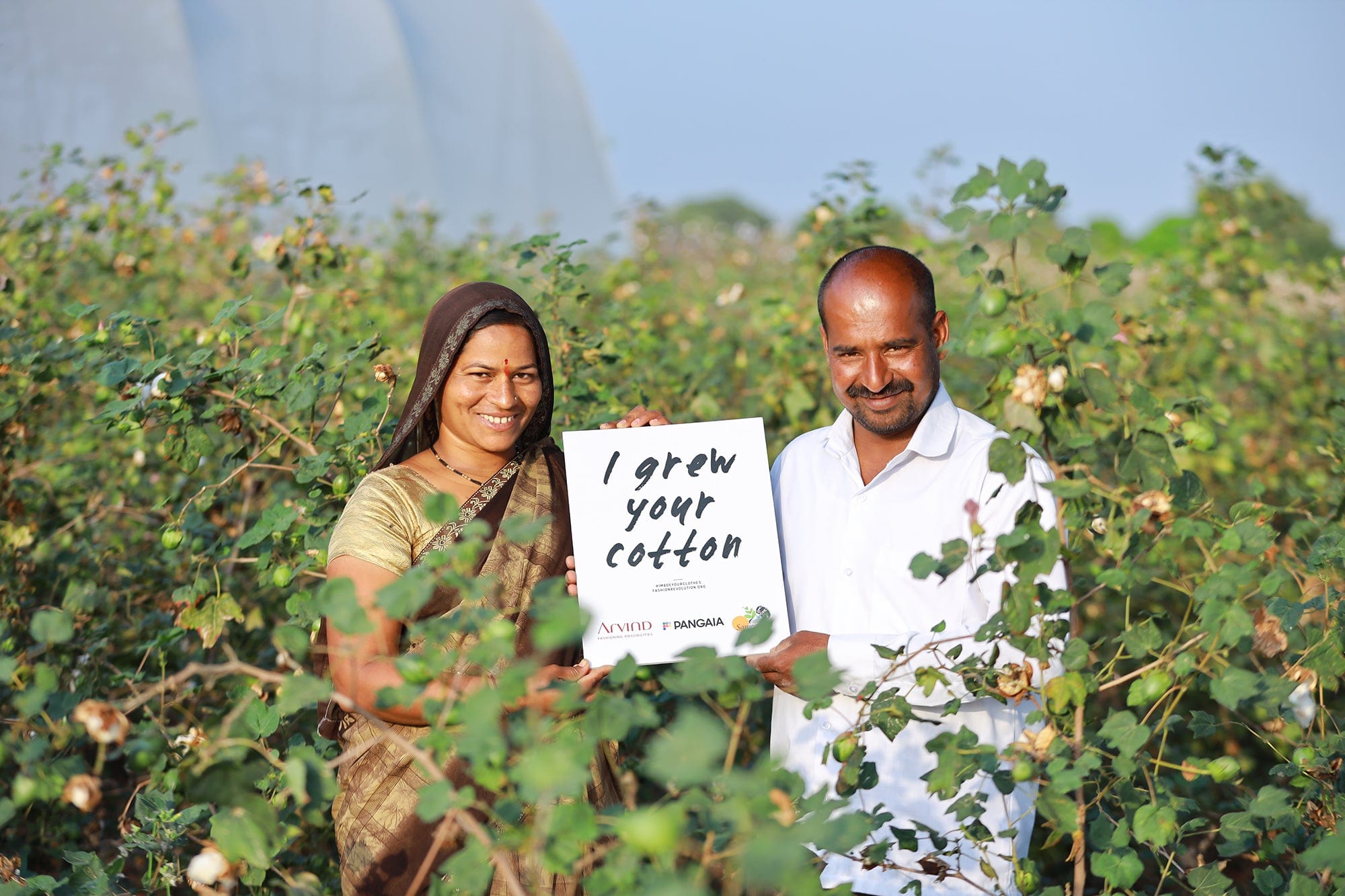 Smiling cotton farmers in green field holding 'I grew your cotton' sign Raw material origin