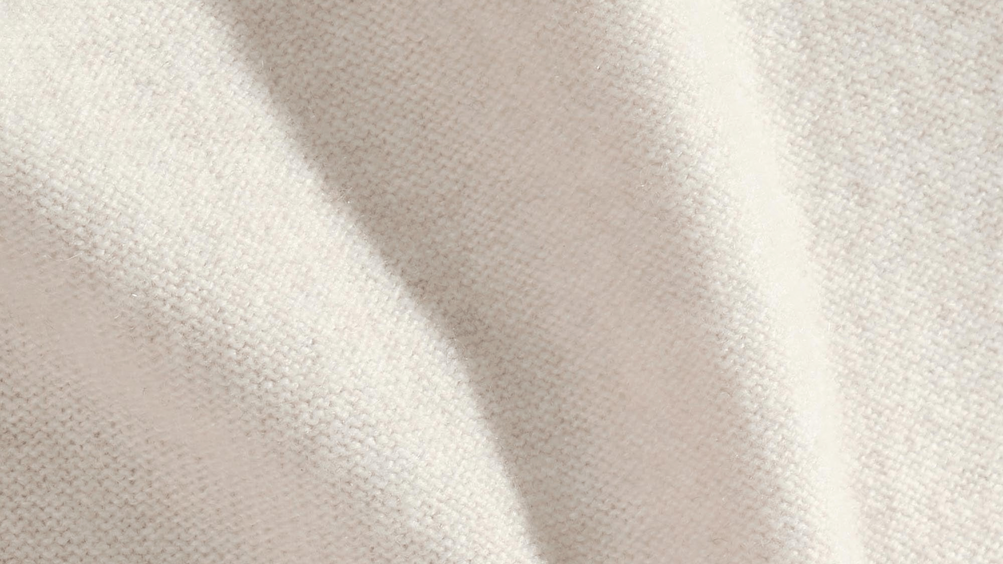 Soft creamy white fine knit fabric texture with gentle drapes. Luxurious garment material close-up
