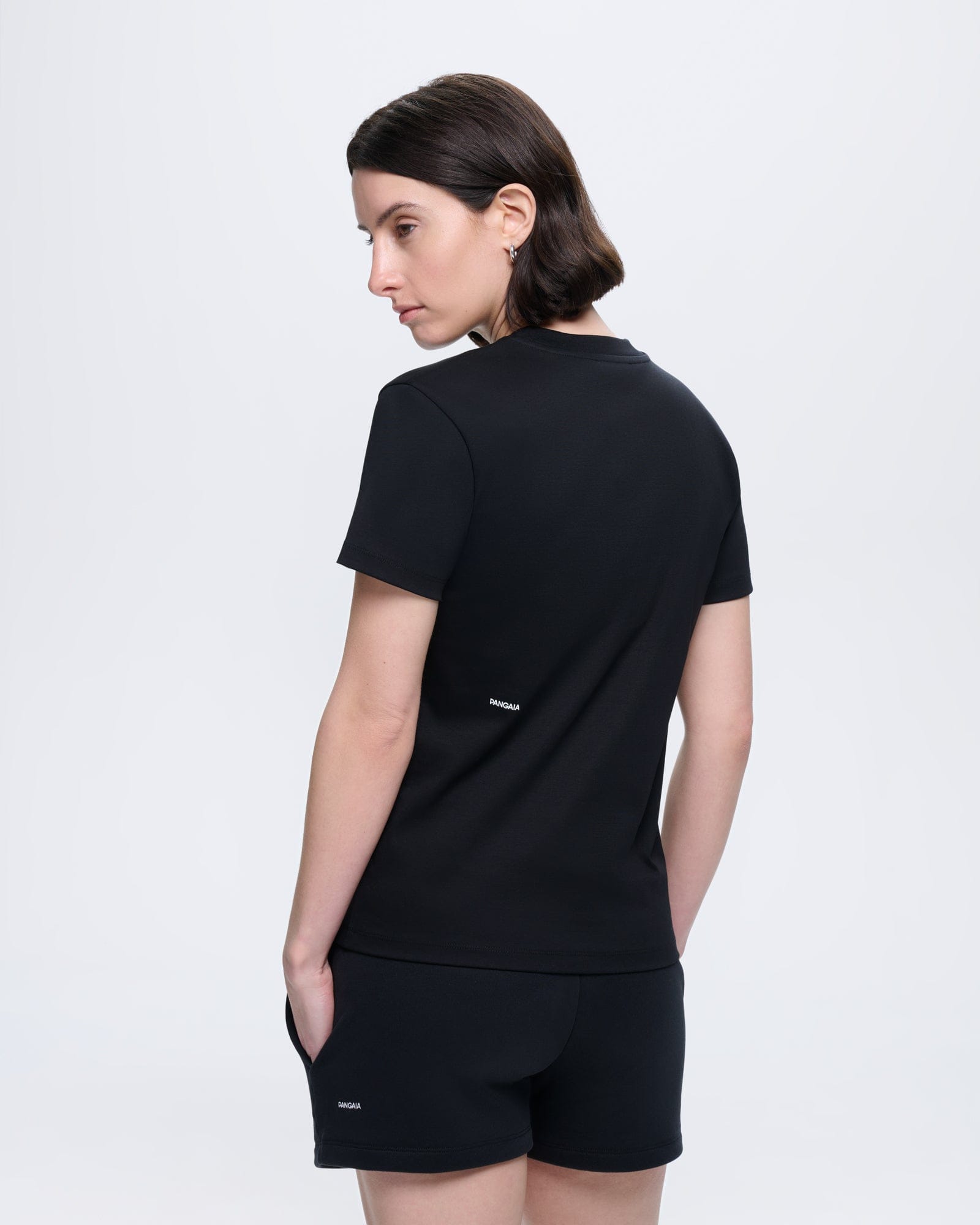 Model wears black Womens Interlock T-Shirt. Organic cotton, regular fit, crew neck. PANGAIA logo on back and shorts
