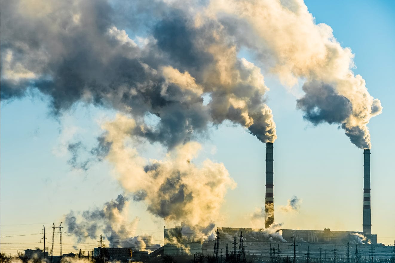 Industrial plant with tall smokestacks emitting dense grey and yellow smoke plumes against a blue sky, an industrial landscape with power lines