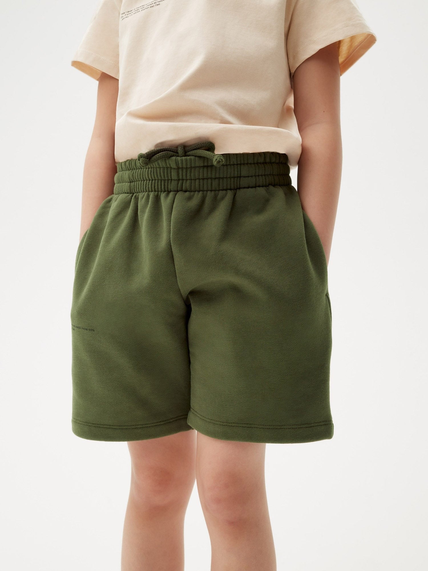 Rosemary green midweight kids' long shorts. 100% organic cotton with elastic drawstring waist and side pockets, worn by child